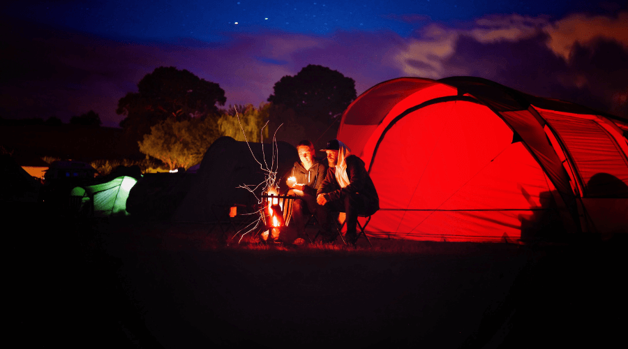 Campers at night in front of a tent. Source: https://www.pexels.com/cs-cz/foto/svetly-krajina-obloha-zapad-slunce-776117/