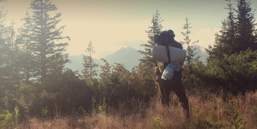 Muž s batohem hledící na les a kopce v pozadí