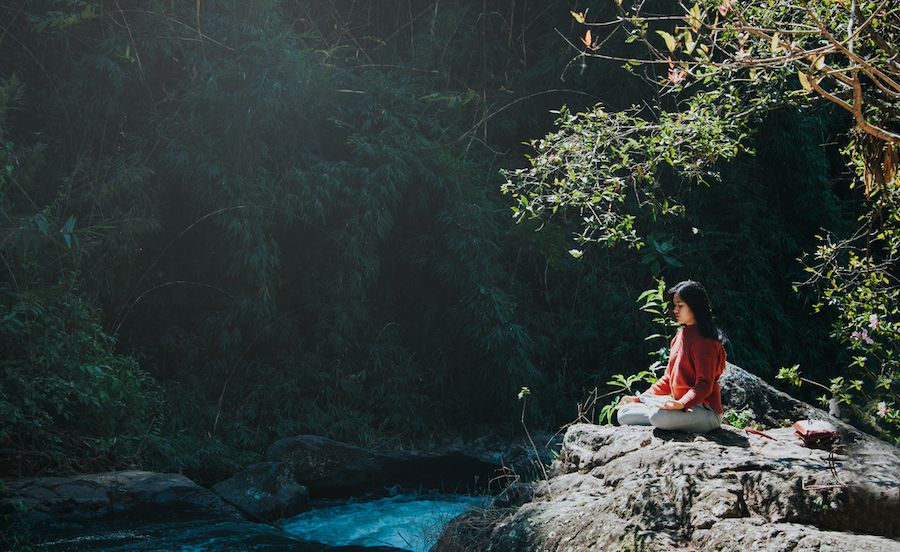 Dievča meditujúce na kameni pri potoku