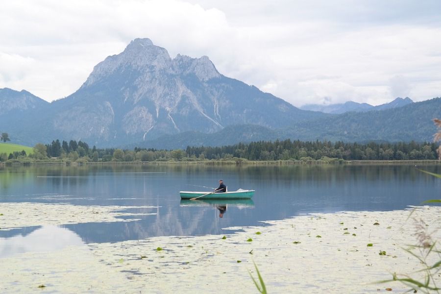 Muž na loďke uprostred jazera medzi horami